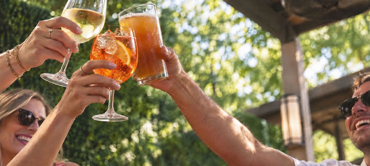Friends raising a glass of wine, a spritz, and a beer on the patio