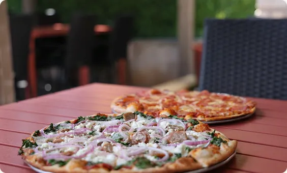 Two brick oven pizzas on a patio table